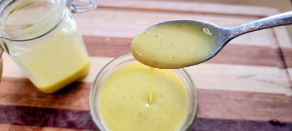 a spoon being dipped and removed from a bowl of lemon vinaigrette salad dressing.