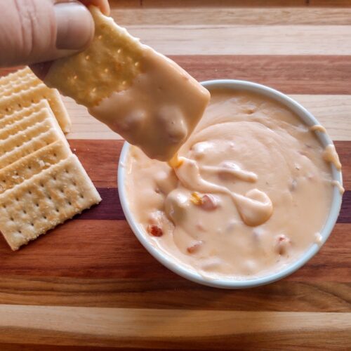 a cracker being dipped into 3 ingredient cheese dip