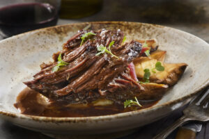 a short rib on a plate with red wine sauce on top.