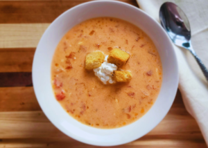 A bowl of 4bs cream of tomato soup in a white bowl with a spoon laying next to it.