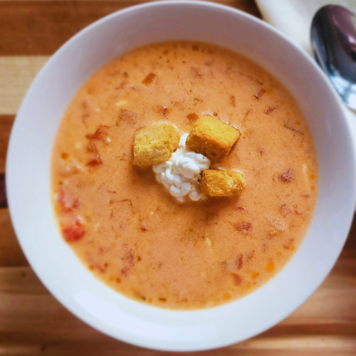 A bowl of 4bs cream of tomato soup in a white bowl with a spoon laying next to it.