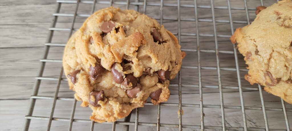 a freshly baked chocolate chip cookie with peanut butter sitting on a cooling rack.