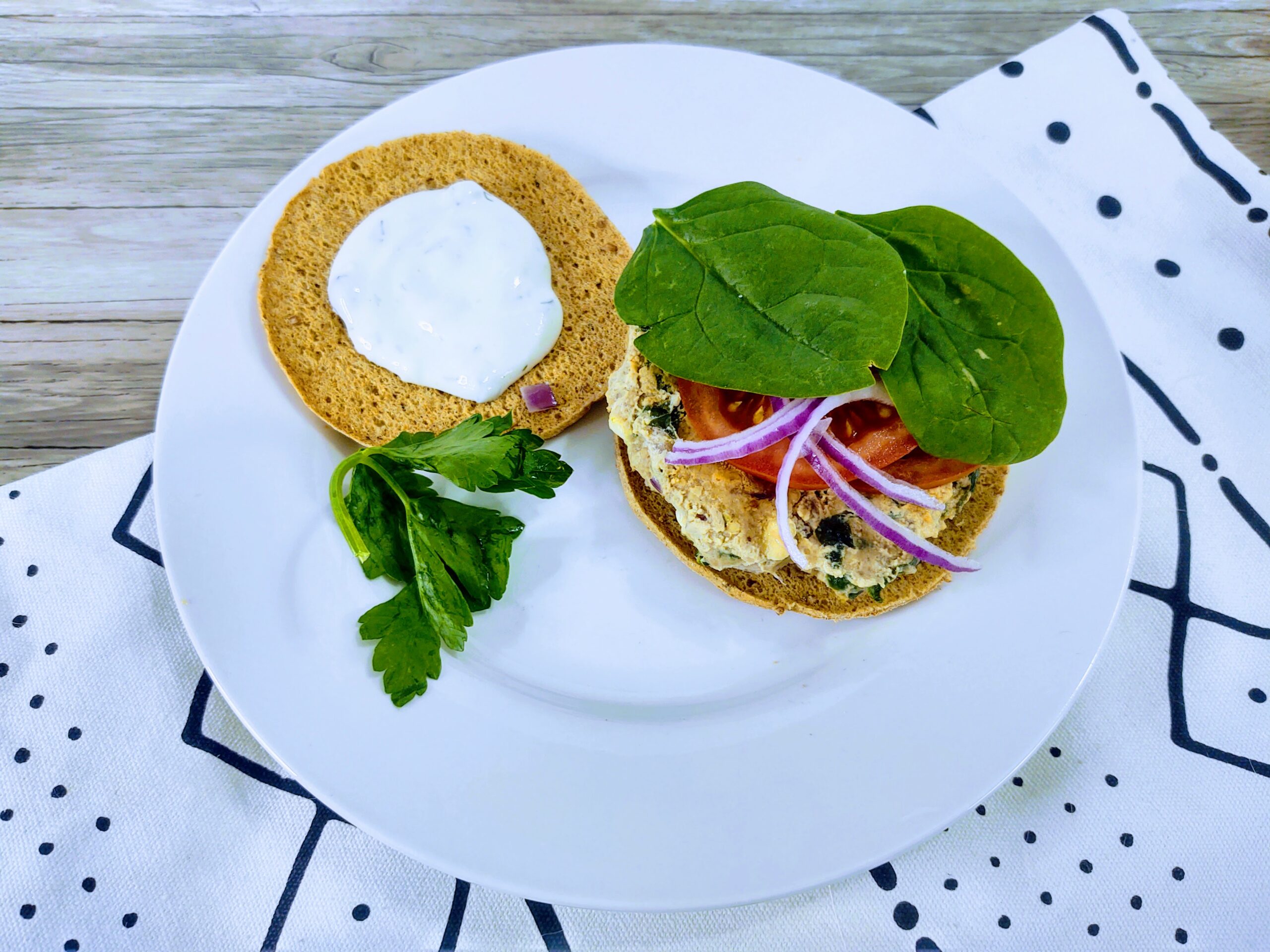 A turkey burger with spinach, tomato, onion and Taziki sauce sitting on a white plate