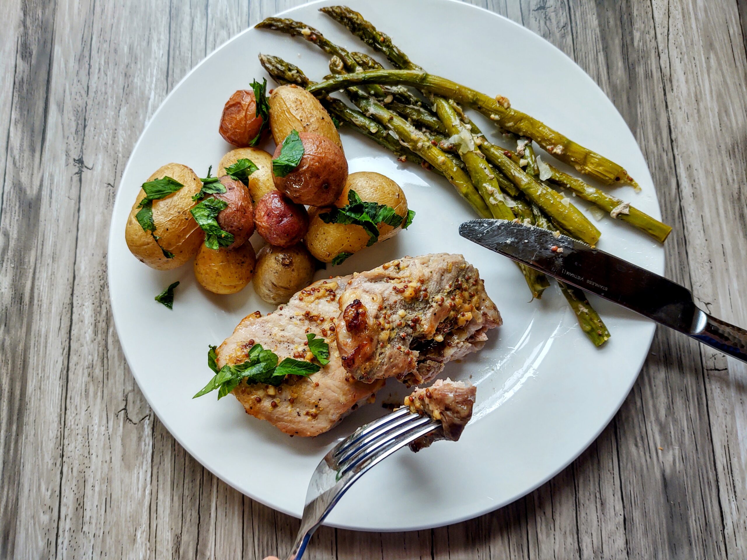cooked boneless pork chop, dutch oven potatoes and roasted asparagus on a white plate