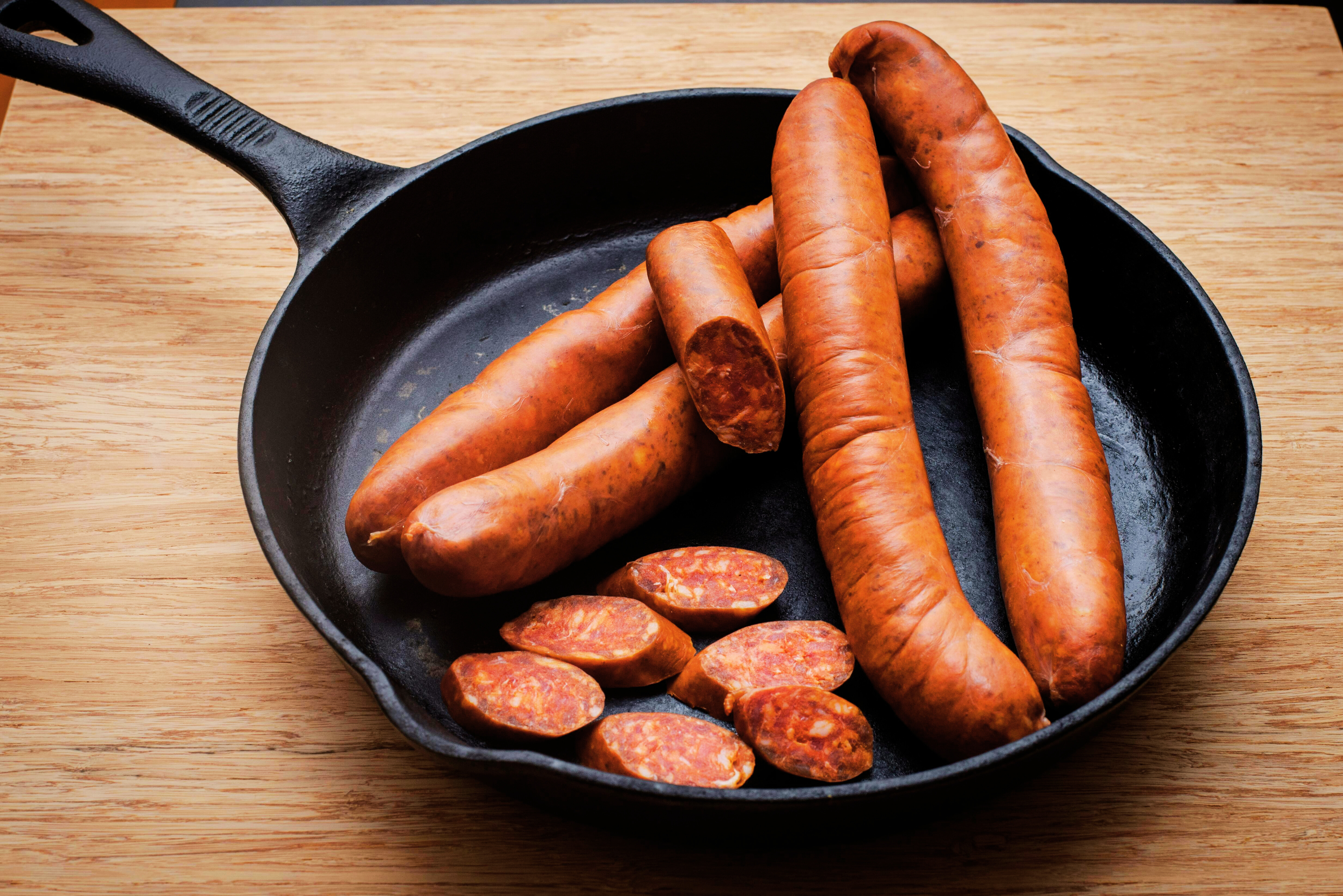 A black cast iron skillet with kielbasa and smoked sausage resting in it.